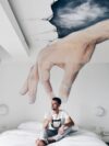 man sitting on bed while holding ceramic mug