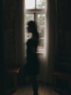 A woman standing in front of a window in a dark room