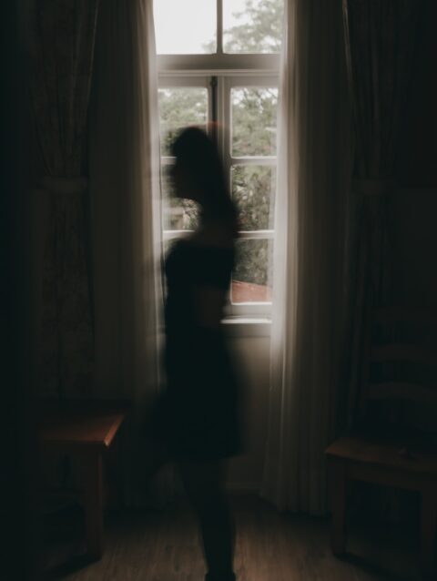A woman standing in front of a window in a dark room