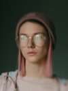 A woman with pink hair wearing glasses and a hat