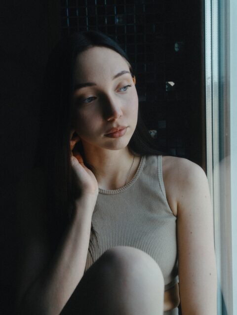 A woman sitting on a window sill next to a window