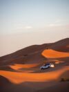 A car driving through the desert with sand dunes in the background