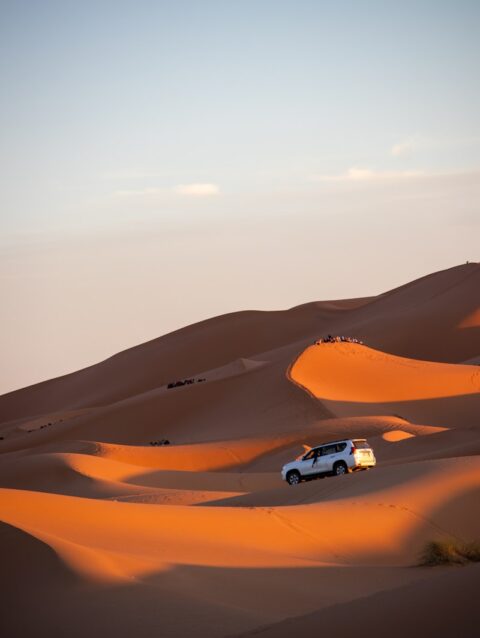 A car driving through the desert with sand dunes in the background