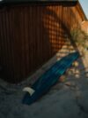 A blue surfboard laying in the sand next to a building
