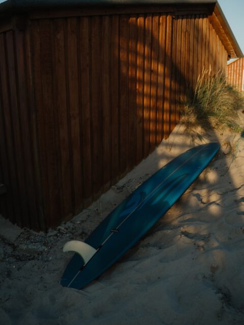 A blue surfboard laying in the sand next to a building